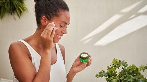 Kvinna smörjer in ansiktet med Weleda Skin Food